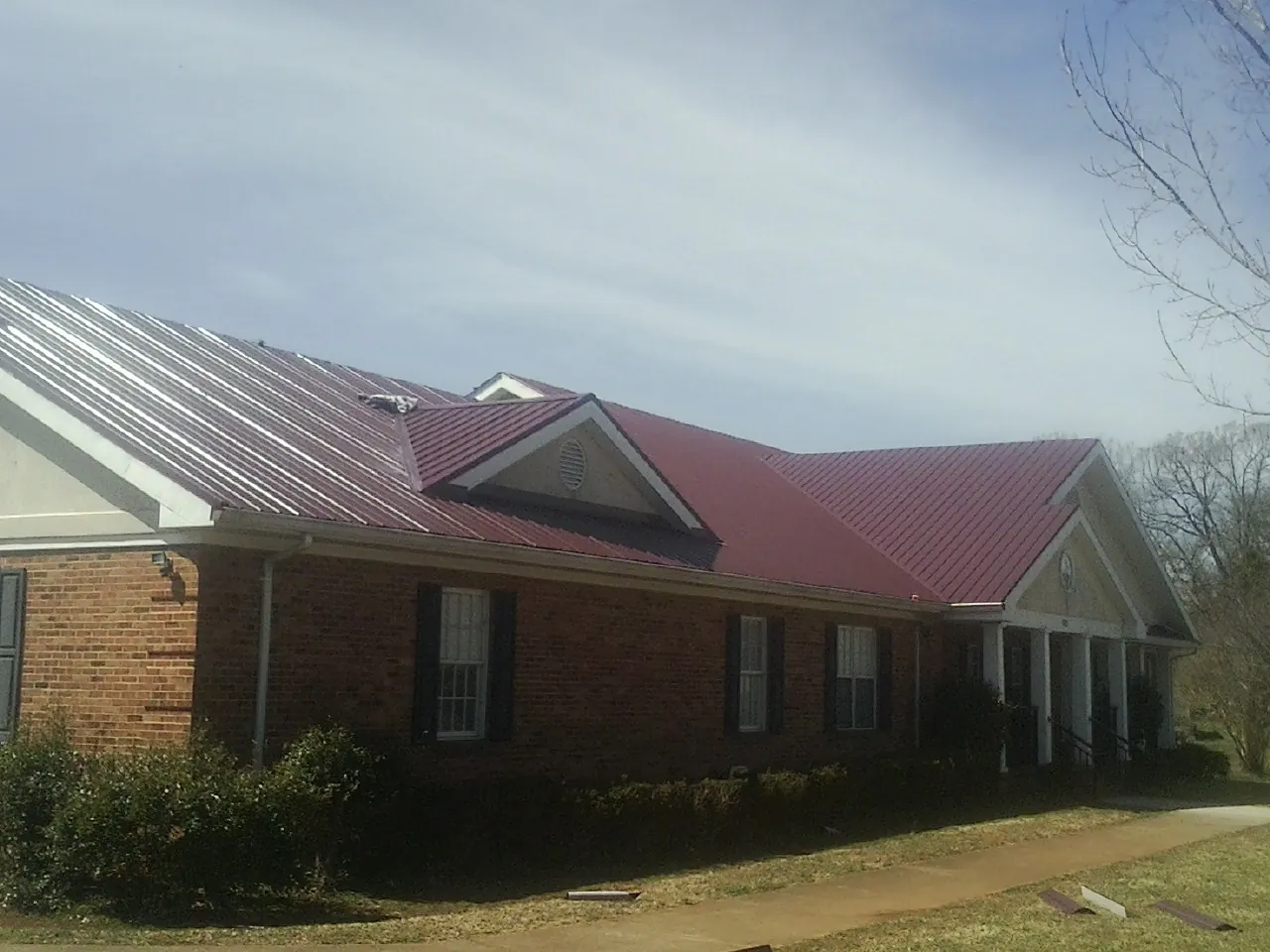Red metal roof with gabled entries on a long brick building, from a Hail Damage Roof Repair job in Sutter