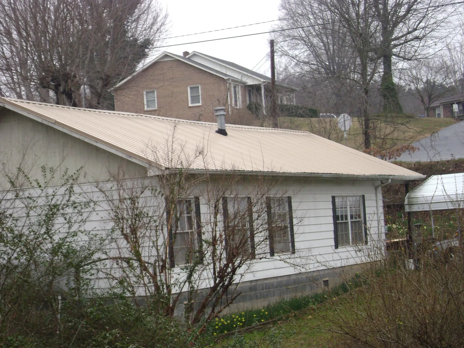 Tan metal roof on a white sided house set into a hillside — Commercial Roofing by Roofing Brothers in Sutter